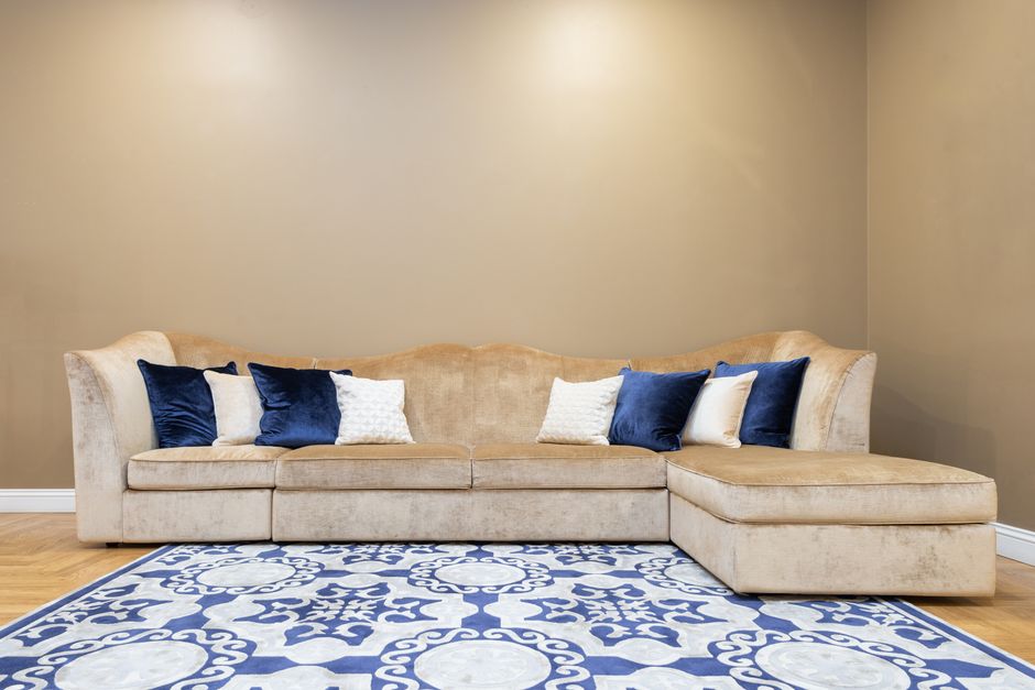 Close-up of a person using a handheld vacuum cleaner to deep clean a green upholstered sofa in a living room, with a background of a grey sofa. The scene is well-lit, highlighting the fabric's texture